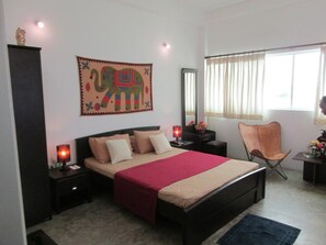 A bedroom with a bed, nightstands, a chair, a mirror, and a window with curtains. - Ripple Reach Apartments (Galle)