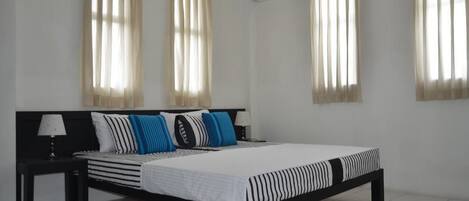 Un dormitorio moderno con estructura de cama negra, ropa de cama blanca y almohadas azules. Hay dos mesitas de noche con lámparas y un equipo de aire acondicionado en la pared.
