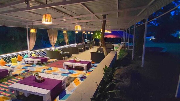 An outdoor seating area with tables and chairs, a checkered floor, and hanging lights. - Hiranya Resorts (Chhatrapati Sambhajinagar)
