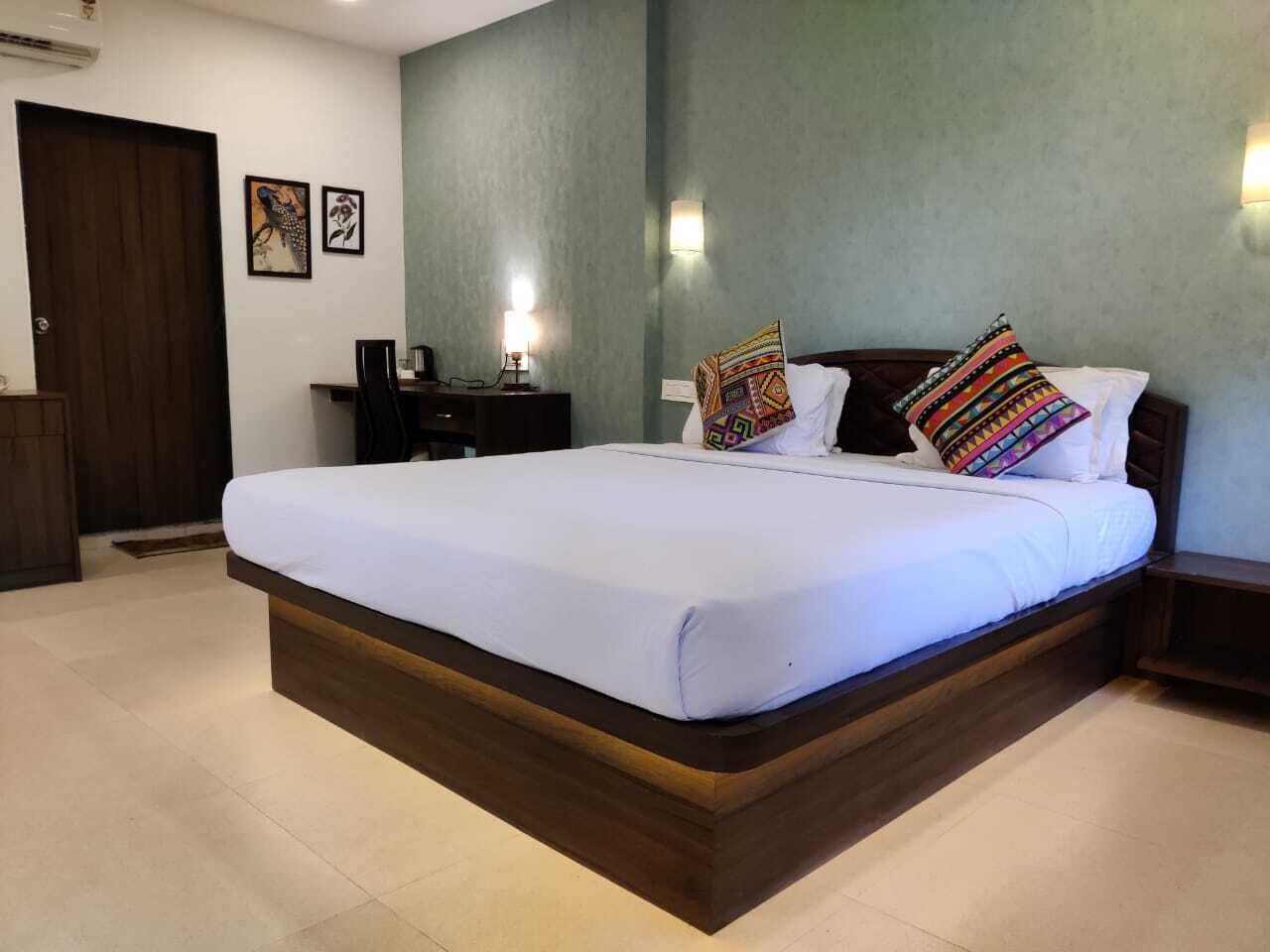 A large bed with a wooden frame, a desk with a chair, and a wall-mounted lamp.