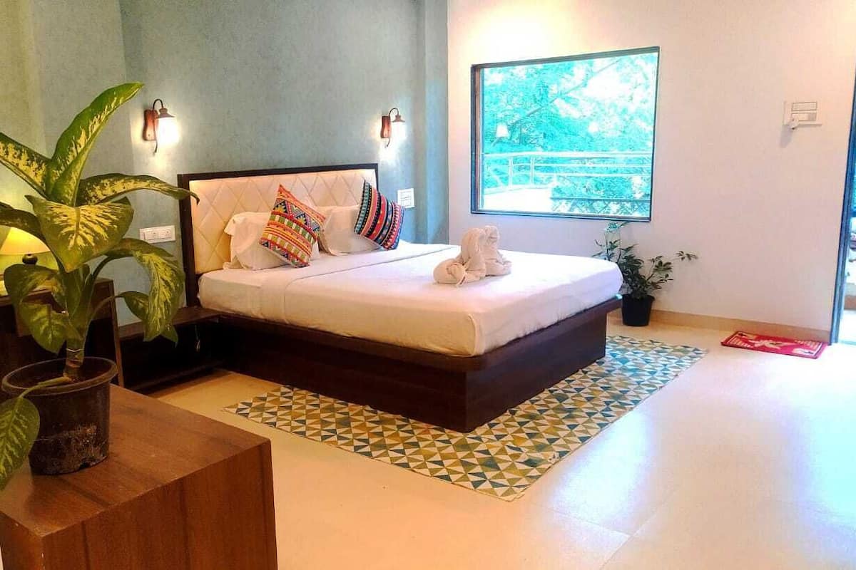 Um quarto com cama, almofadas, uma planta em vaso e janela com vista.