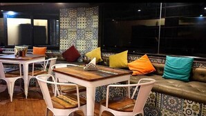 A cozy seating area with a patterned wall, a wooden table, and colorful cushions. - Hiranya Resorts (Chhatrapati Sambhajinagar)