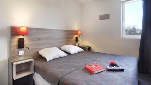 A neatly made bed with two pillows, a bedside table with a lamp, and a window with curtains. - Chalet in Praroustan with Stunning Mountain Views (PRA LOUP 1500)