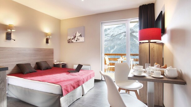 A hotel room with a bed, a desk, a chair, a table with breakfast items, a painting on the wall, and a window with a mountain view. - Chalet in Praroustan with Stunning Mountain Views (PRA LOUP 1500)