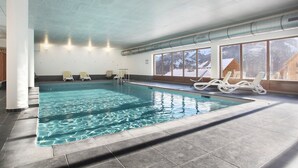 An indoor swimming pool with clear water, surrounded by lounge chairs and large windows. - Chalet in Praroustan with Stunning Mountain Views (PRA LOUP 1500)