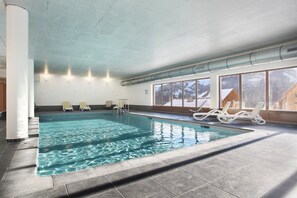 Ein Innenpool mit klarem Wasser, umgeben von Liegestühlen und großen Fenstern.