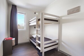 A bunk bed room with a window, a bedside table, and a wall-mounted light fixture.
