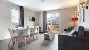 A modern living room with a dining area, a sofa, a coffee table, and a TV mounted on the wall. - Chalet in Praroustan with Mountain Views (PRA LOUP 1500)