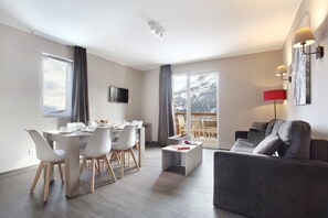 Ein modernes Wohnzimmer mit Essbereich, einer Couch, einem Couchtisch und einem an der Wand befestigten Fernseher.