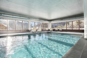 Ein Hallenbad mit klarem Wasser, großen Fenstern und Liegestühlen.