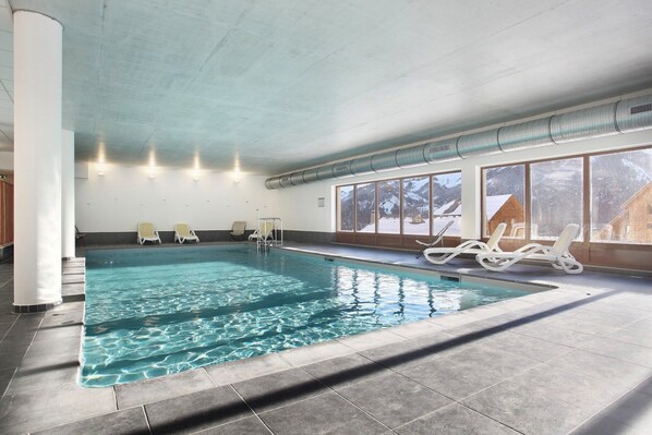 An indoor swimming pool with clear water, surrounded by lounge chairs and large windows. - Chalet in Praroustan with Mountain Views (PRA LOUP 1500)