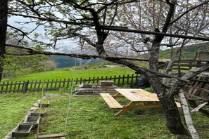 A picnic area with wooden benches and a rope swing, surrounded by a wooden fence and trees. - Chalet in Praroustan with Mountain Views (PRA LOUP 1500)
