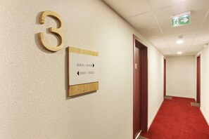 Ein Flur mit Hinweisschildern für Zimmer 3, Pfeilen zur Orientierung und Notausgangsschildern.