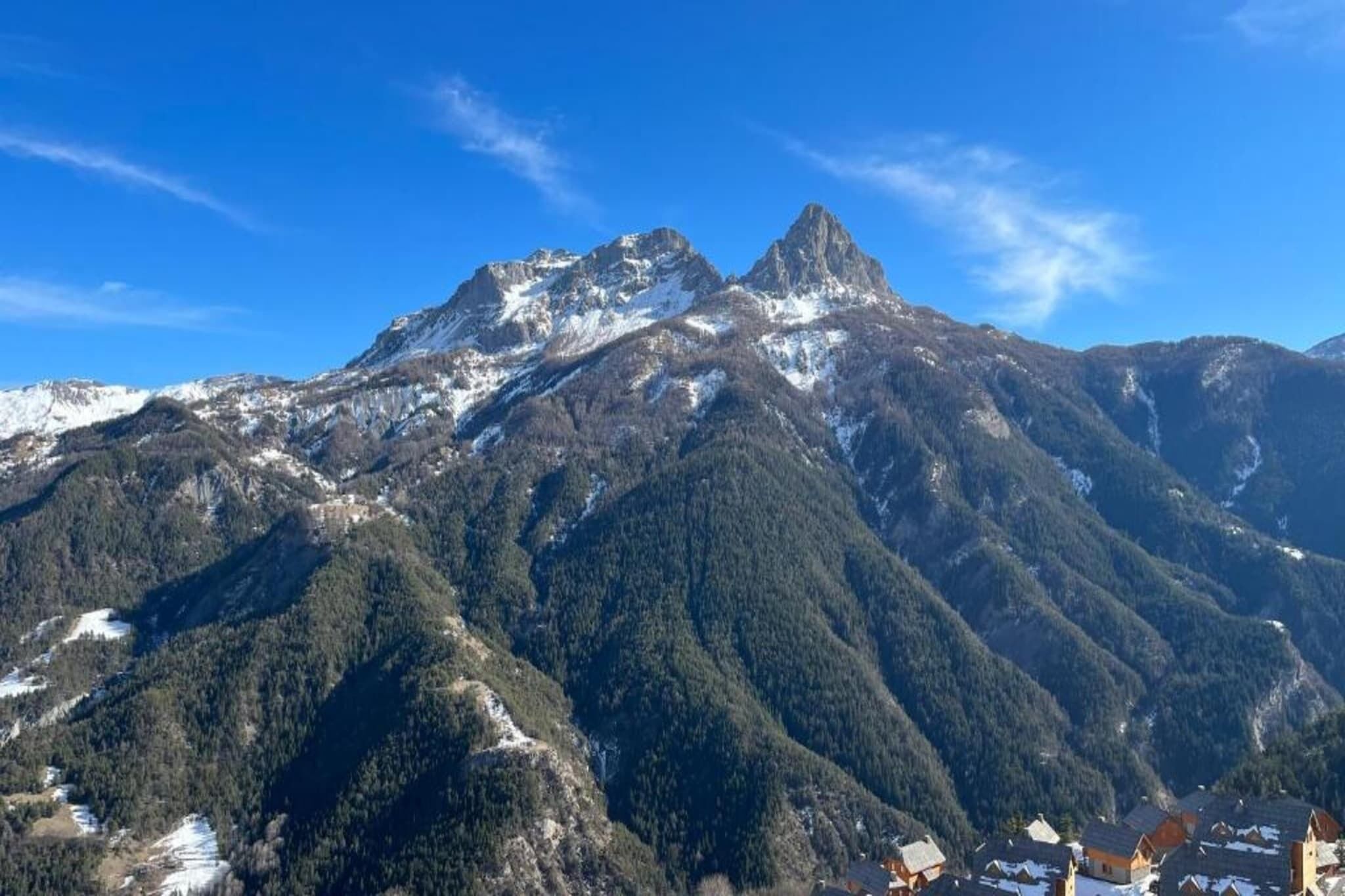 A mountain landscape with a prominent peak, forested slopes, and a small settlement at the base.