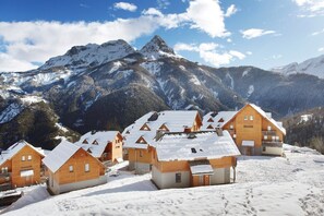 A cluster of wooden cabins with snow-covered roofs, set against a backdrop of snow-capped mountains and a clear sky. - Chalet in Praroustan with Mountain Views (PRA LOUP 1500)