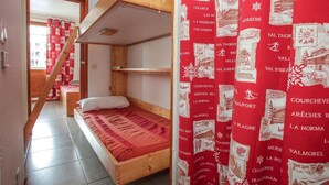 Ein Zimmer mit einem Etagenbett, einer Holztreppe und einem roten, gemusterten Vorhang.