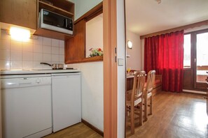 A compact kitchen with a microwave, stove, and washing machine. A dining area with wooden chairs and a table is visible through an open door. - Tignes Chalet for Families (Tignes)