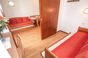A compact room with a wooden floor, a bed, a sofa, and a small table with a chair.