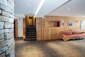 A wooden interior with a stone wall, a staircase, and a bed with plaid bedding. - Tignes Chalet for Families (Tignes)