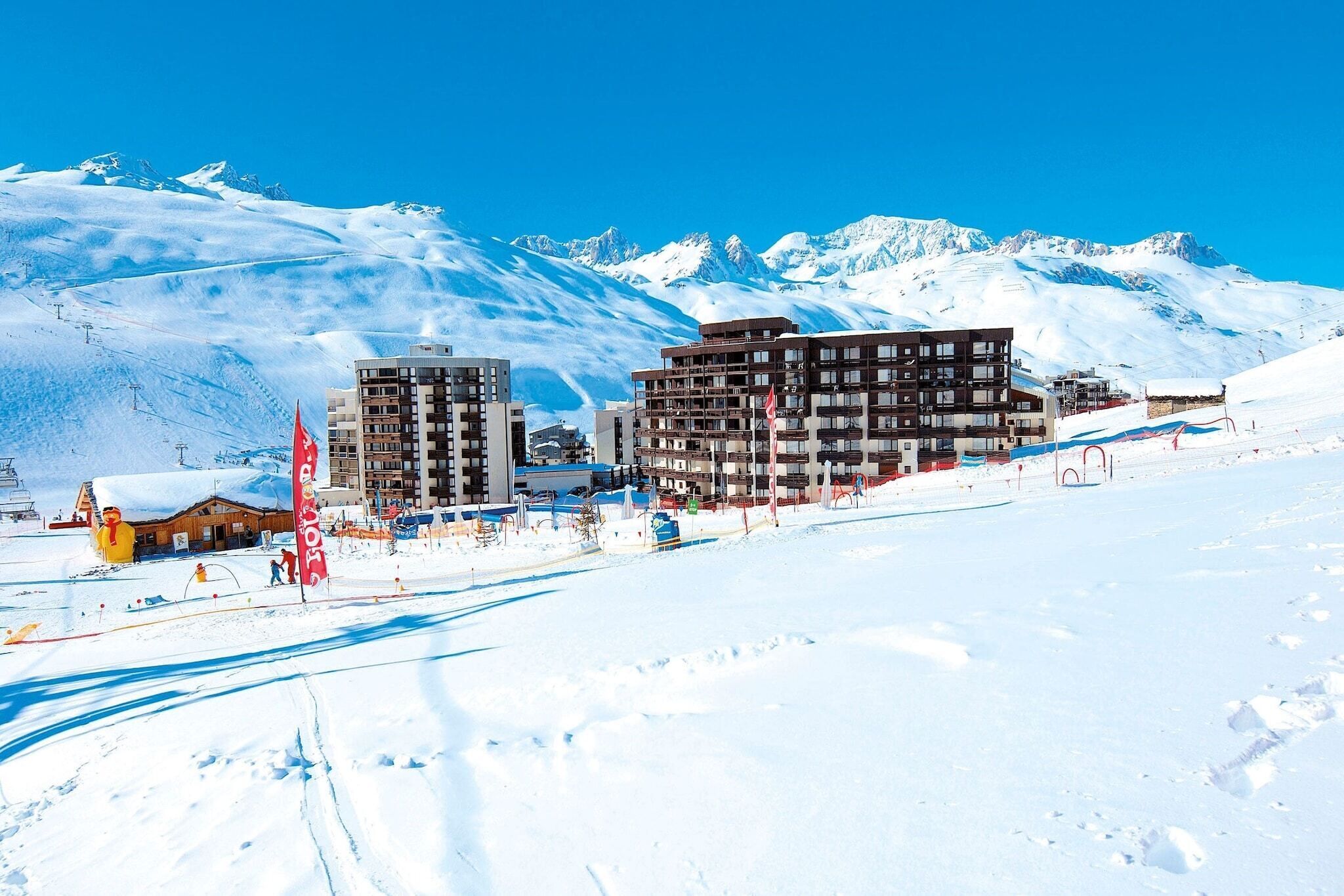 En snötäckt skidort med moderna byggnader, skidliftar och en klar, blå himmel.