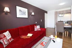 A modern living room with a red sofa, a coffee table, and a dining area with a breakfast setup.