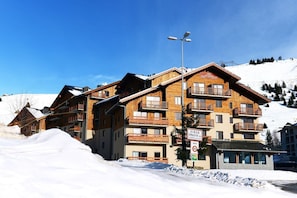 Un edificio de madera de varios pisos con balcones, probablemente un hotel o una posada, rodeado de nieve y árboles.