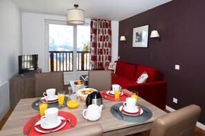 Un comedor con una mesa dispuesta para el desayuno, un sofá y un televisor en una esquina.