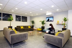 Ein moderner Wartebereich mit grauen Sofas, einem Fernseher und Topfpflanzen.