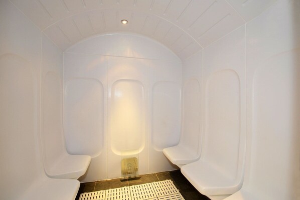 A modern bathroom with three separate urinals, a central light fixture, and a tiled floor.