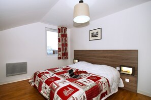 Un dormitorio con una cama, una ventana, un radiador, una lámpara fijada a la pared y un cuadro enmarcado.