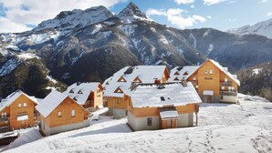 A cluster of wooden cabins with snow-covered roofs, set against a backdrop of snow-capped mountains and a clear sky. - Chalet in Praroustan with Mountain Views (PRA LOUP 1500)