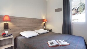 A hotel room with a bed, two bedside lamps, a window with a view, and a book on the bed. - Chalet in Praroustan with Mountain Views (PRA LOUP 1500)