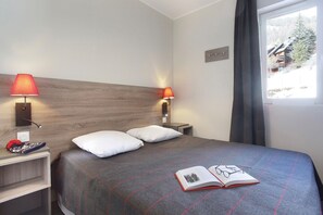 Ein Hotelzimmer mit einem Bett, zwei Nachttischlampen, einem Fenster mit Blick und einem Buch auf dem Bett.