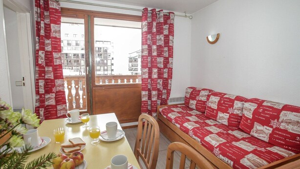 A dining area with a table set for breakfast, a sofa with patterned cushions, and a view of buildings through a window. - Chalet-Style Stay in Val Claret (Tignes)