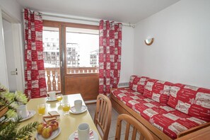 A dining area with a table set for breakfast, a sofa with patterned cushions, and a view of buildings through a window.