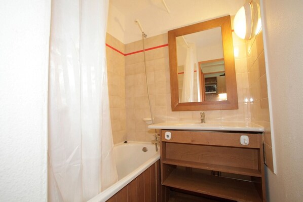 A bathroom with a bathtub, a wooden vanity, a mirror, and a shower.