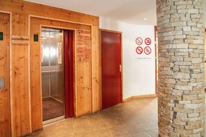 Ein hölzerner Aufzug mit roter Tür, einem Empfangsschild und Schildern mit Rauchverbot und Essensverbot an der Wand.