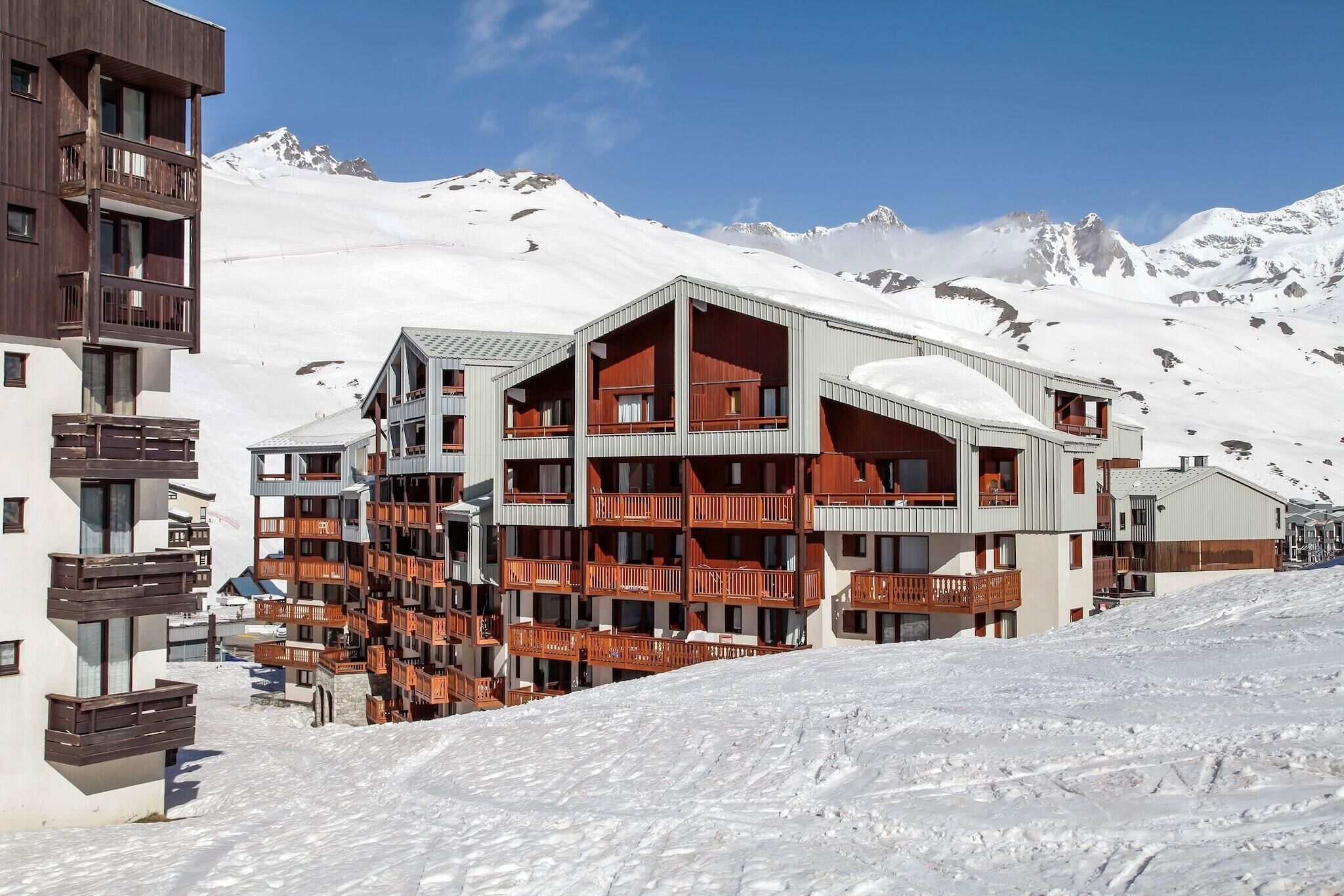 A multi-story hotel with balconies, set against a snowy mountain backdrop.