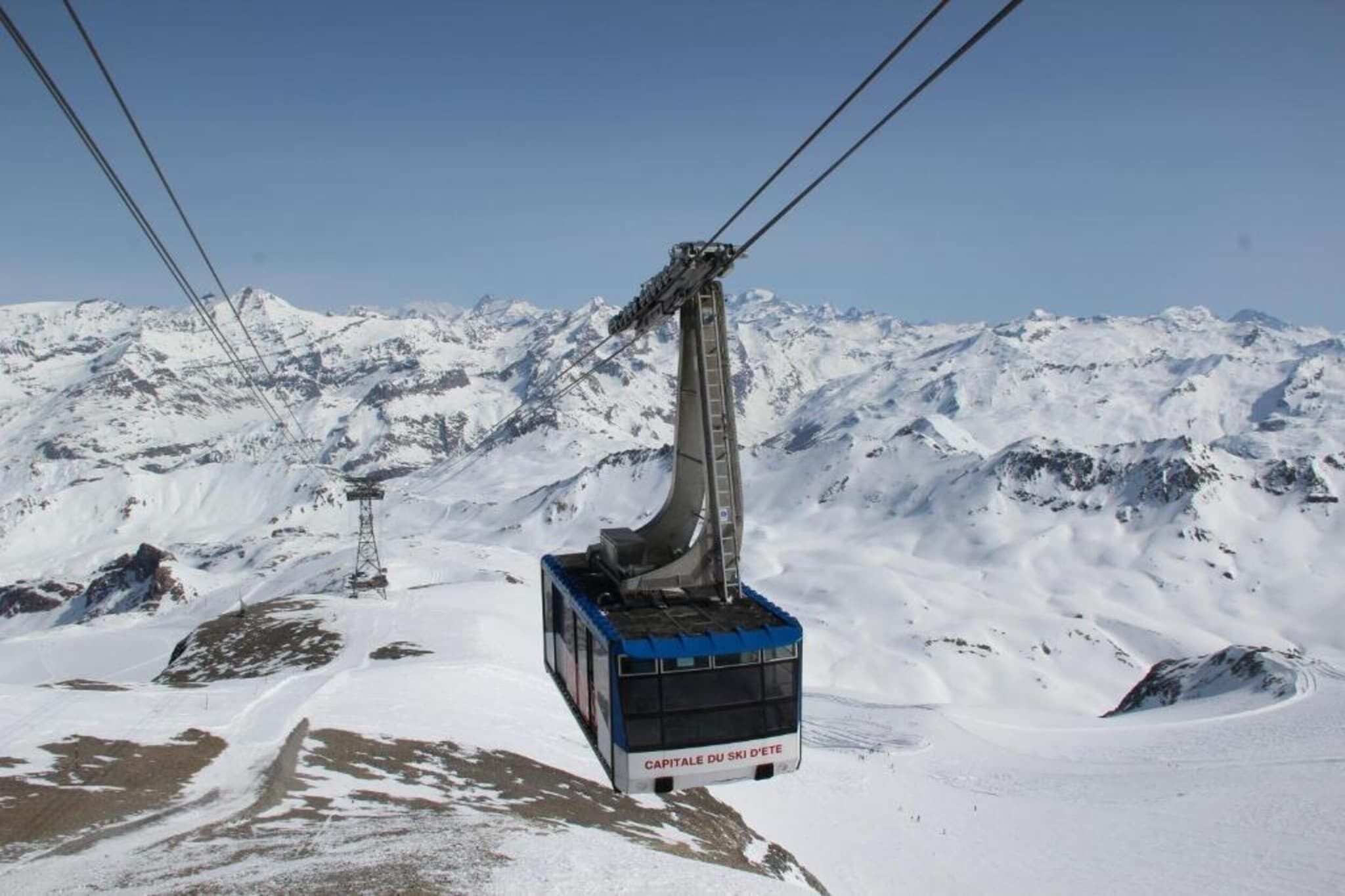 Un téléphérique qui monte une montagne enneigée, sous un ciel dégagé.