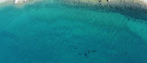 Luchtbeeld van een strand met helder turquoise water en een rotsachtige kustlijn.