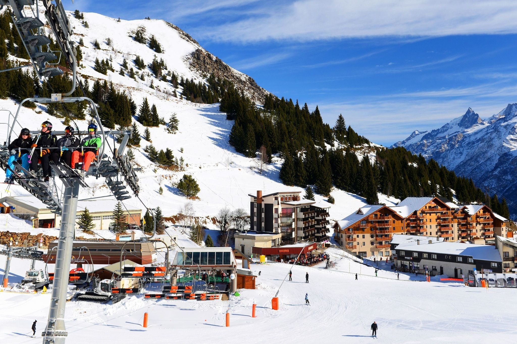 A ski lift with skiers, a snow-covered mountain, and a town with buildings in the background.