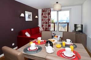 A dining area with a red sofa, a TV, and breakfast items on the table. - Alpine Stay with Balcony (Auris en Oisans)