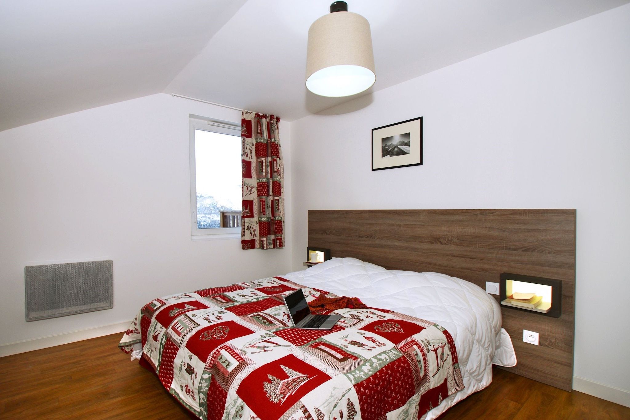 Ein Schlafzimmer mit einem Bett, einem Fenster, einer Heizung, einer Wandleuchte und einem gerahmten Bild.