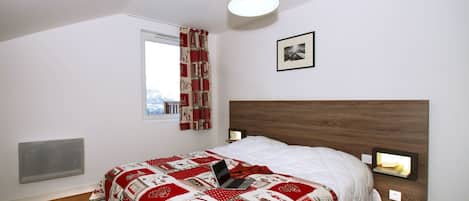 Een slaapkamer met een bed, een raam, een radiator, een wandlamp en een lijst met een afbeelding.