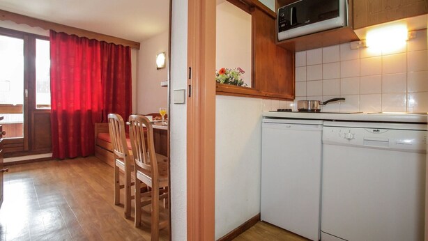 A compact kitchen with a microwave, dishwasher, and a dining area with wooden chairs and a table. - Chalet in French Alps with Alpine Charm (Tignes)