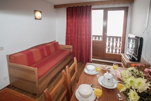 A room with a wooden sofa, a dining table set with plates, glasses, and a TV. - Chalet in French Alps with Alpine Charm (Tignes)