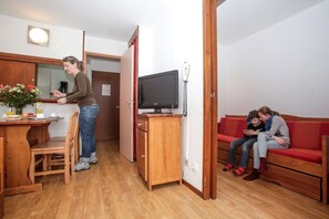 A compact living space with a kitchenette, a wooden cabinet, a television, and a red sofa.