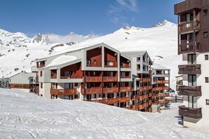 A multi-story hotel with balconies, set against a snowy mountain backdrop.