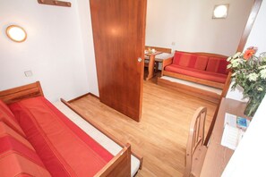 A compact room with a bed, a sofa, a small table, and a wooden door. - Chalet in French Alps with Alpine Charm (Tignes)