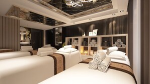 A modern spa room with two massage tables, a decorative ceiling, and a wall with shelves holding towels and toiletries. - S Central Hotel & Spa (Hanoi)